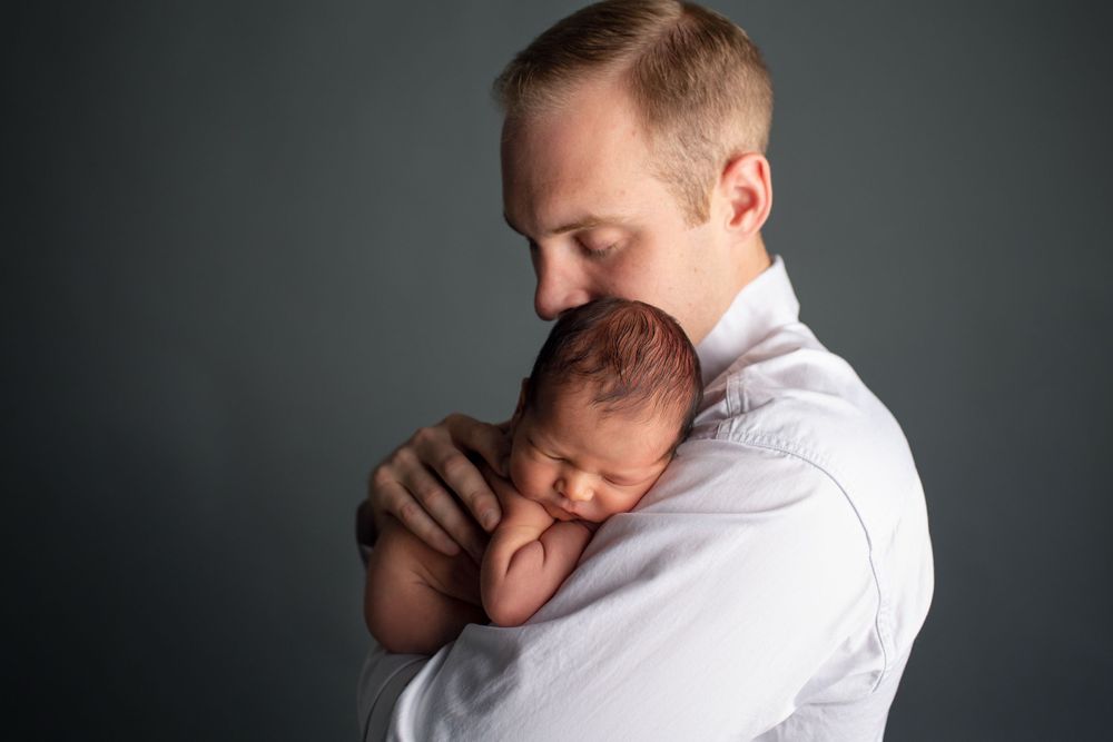 A tender moment captured as parent cradles sleeping newborn against gray studio backdrop.