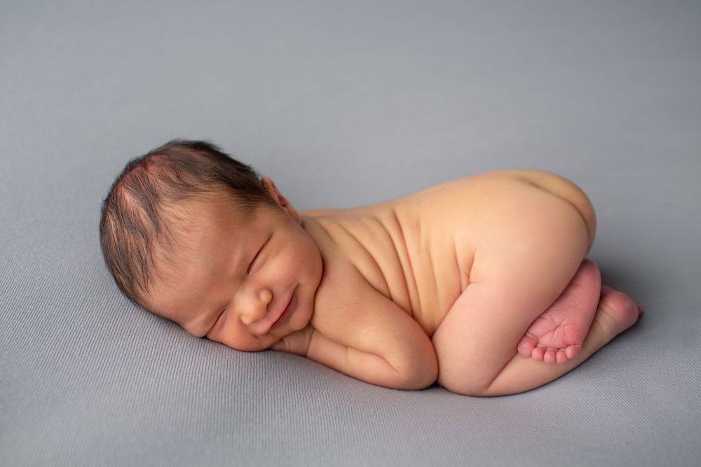 Peaceful sleeping newborn baby curled up on soft gray blanket.