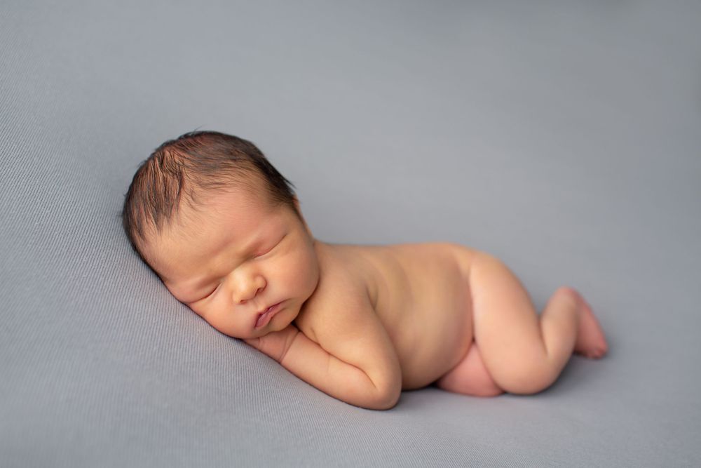Serene newborn baby sleeping on side against gray backdrop.