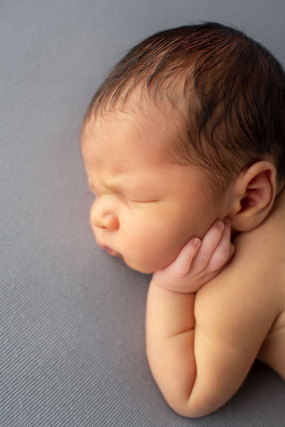 Sweet sleeping newborn with hand under cheek on textured gray background.