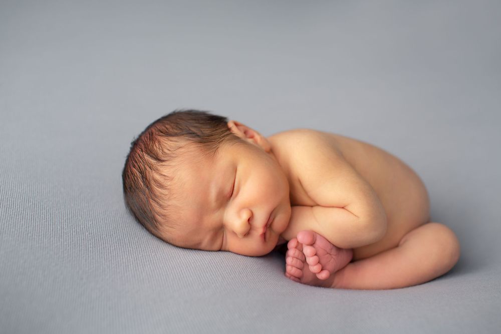 Peaceful sleeping newborn curled up on soft gray backdrop.