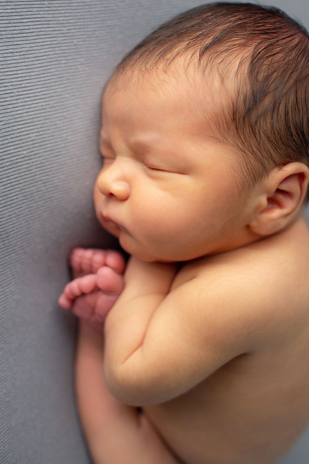 Close-up profile of sleeping newborn baby against gray textile background.