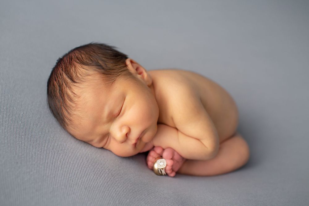 Sleeping newborn baby curled up peacefully on soft gray fabric backdrop during professional photo session.