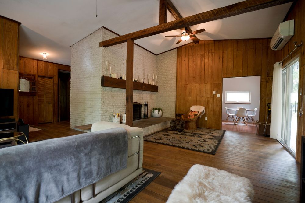 Spacious living room with exposed wooden beams, gray sofa, and rustic fireplace.