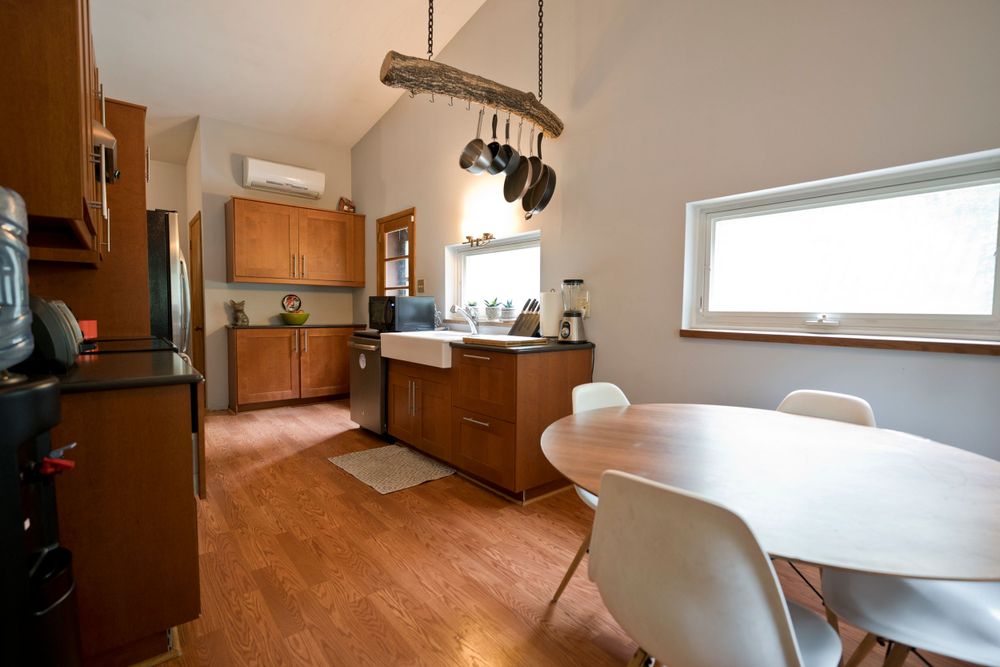 Modern kitchen with wooden cabinets, vaulted ceiling, and white round dining table on hardwood floors.