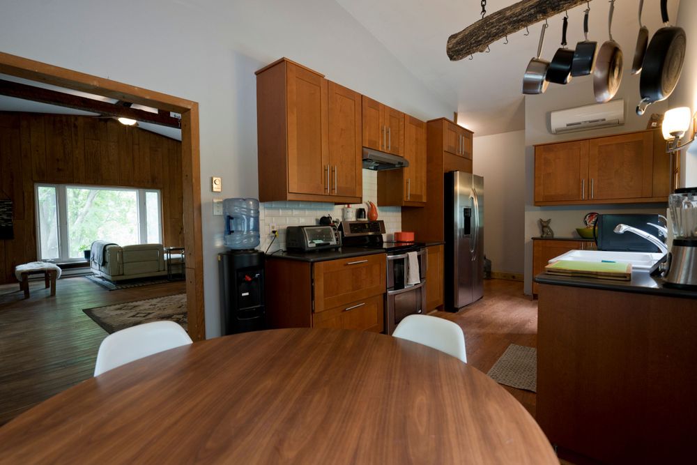 Open concept kitchen with wooden table, white chairs, and hanging pot rack under vaulted ceiling.