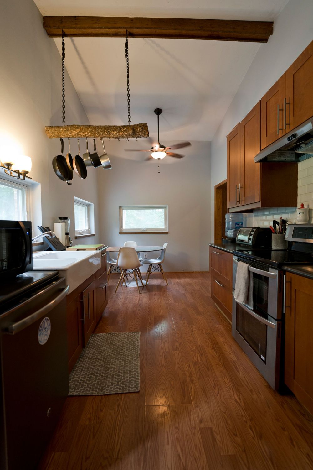 Long galley kitchen with rustic pot hanger, modern appliances, and hardwood flooring.