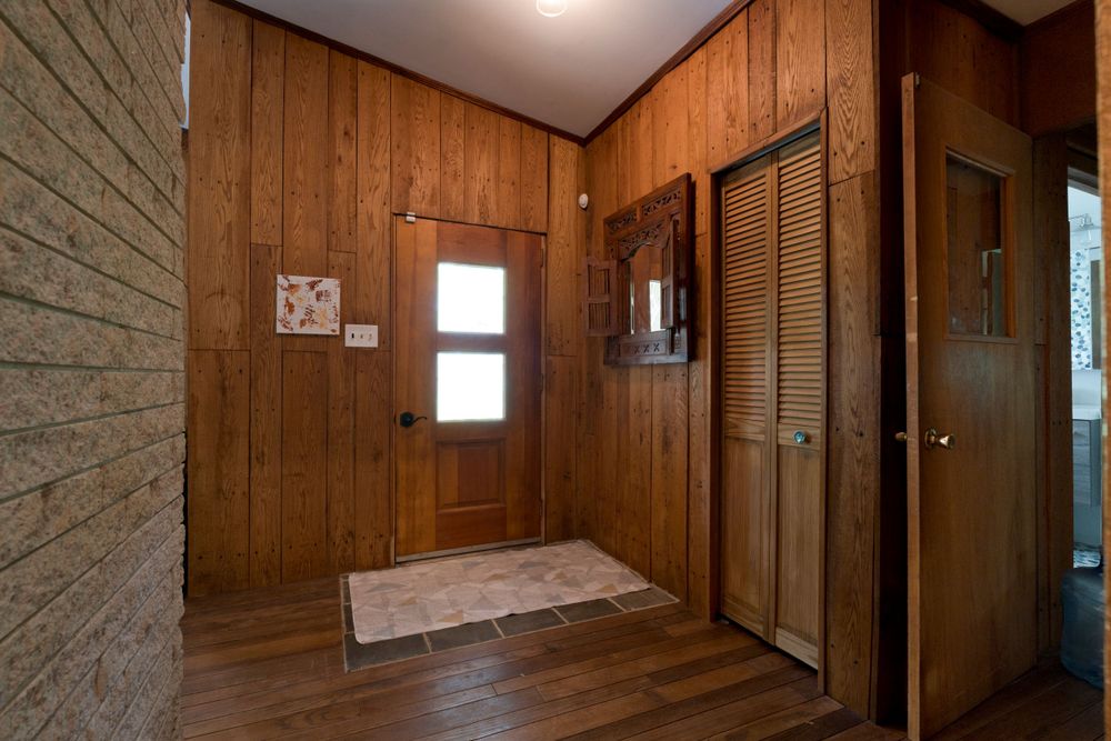 Wood-paneled entryway with hardwood floors and natural lighting through small window.