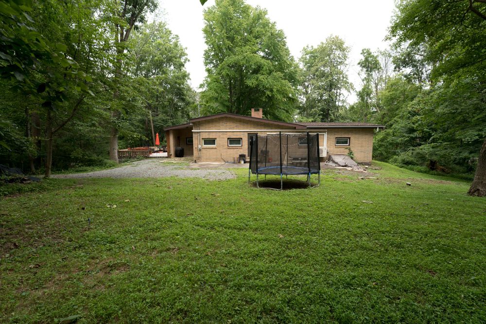 Modern ranch house with trampoline in spacious backyard surrounded by trees.