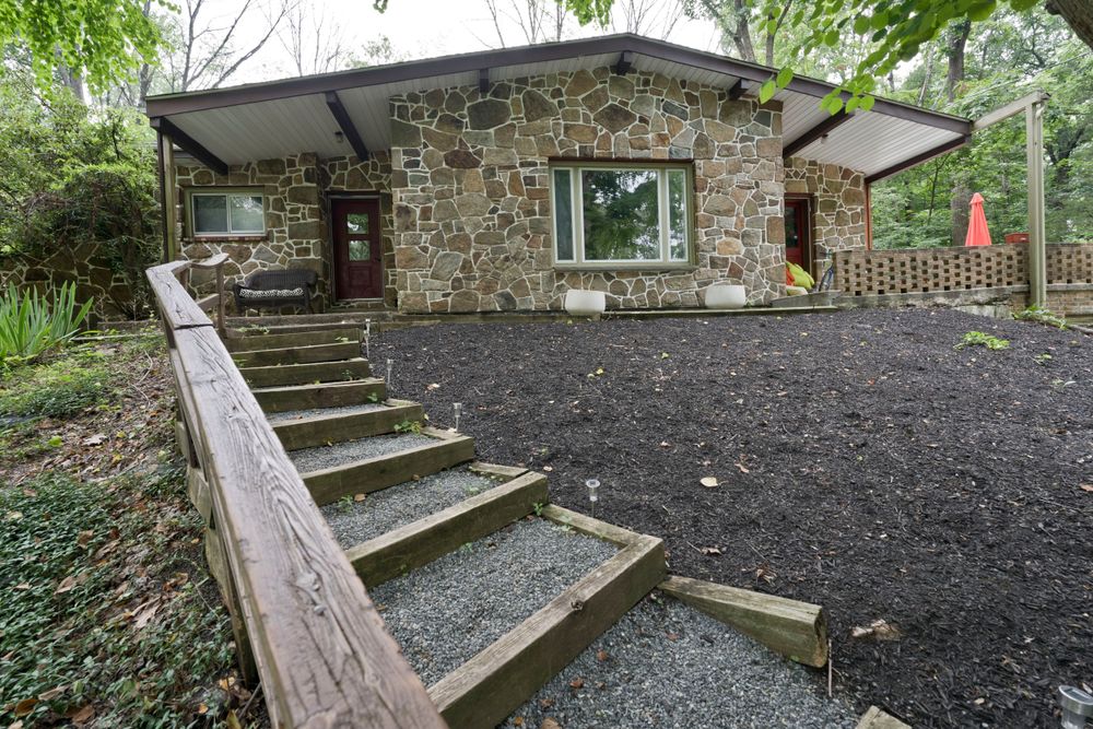Stone facade house with wooden steps and dark mulch landscaping surrounded by forest.