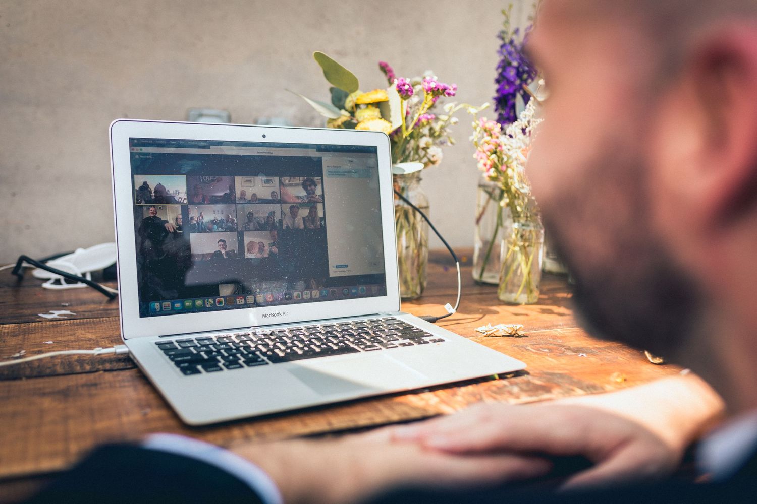 Laptop displaying a video call with flowers in vases on wooden desk.