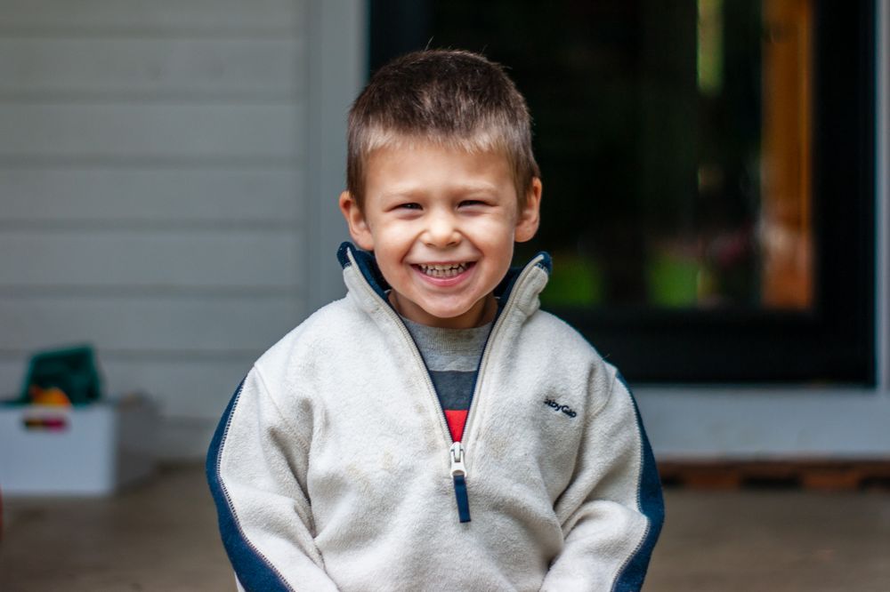 Young boy on porch of family home smiling in Clintonville, Ohio by Jamie Macey Photography