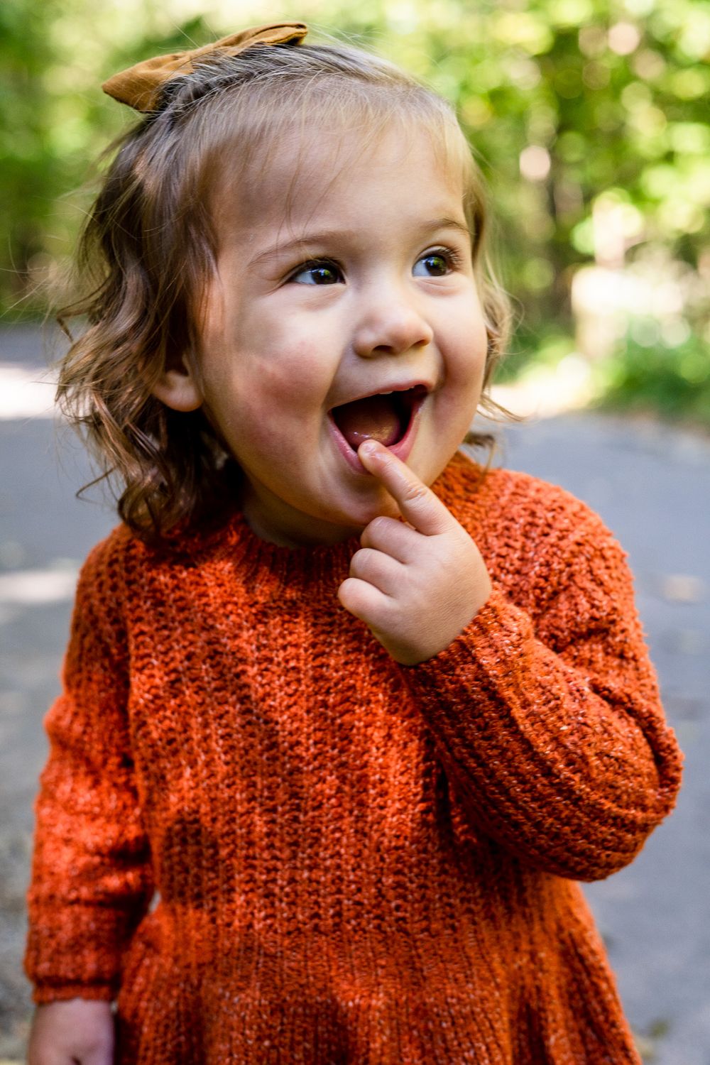 Young girl smiling and touching lip with tree foliage around in Clintonville, Ohio by Jamie Macey Photography