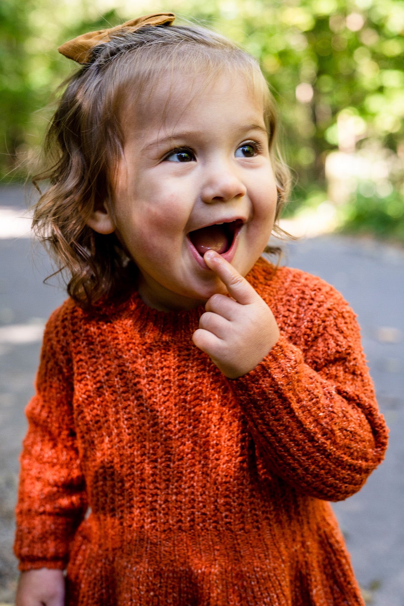 Young girl smiling and touching lip with tree foliage around in Clintonville, Ohio by Jamie Macey Photography