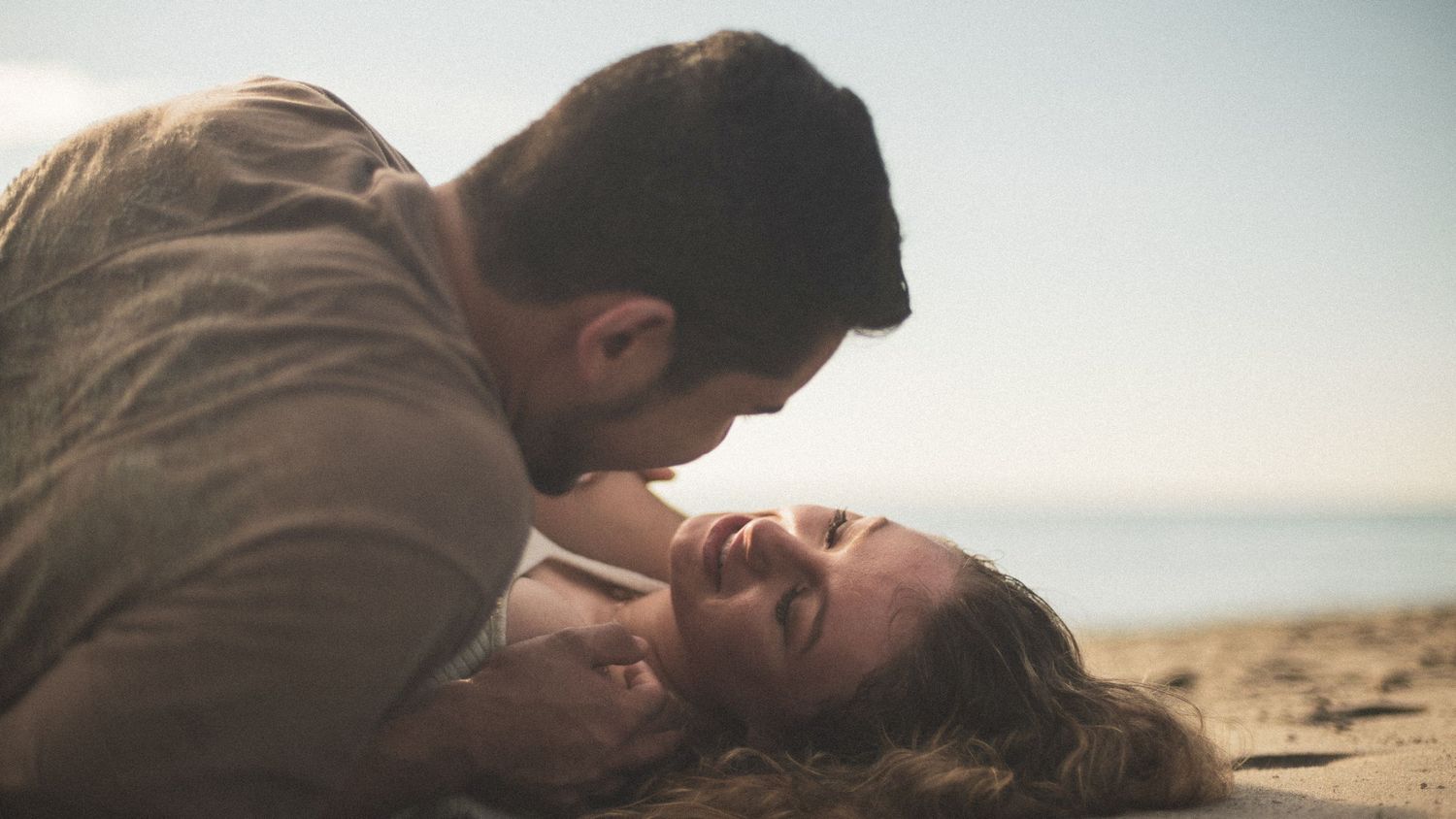 A romantic moment captured between a couple lying on a beach at sunset.