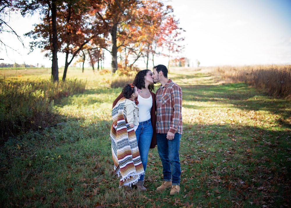 Couple sharing a kiss in an autumn field surrounded by colorful fall foliage.