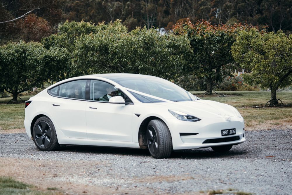 White Tesla Model S limousine parked on gravel driveway for wedding transportation.