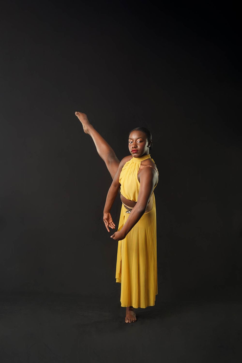 A dancer in a flowing yellow dress strikes an elegant pose against a dark background.