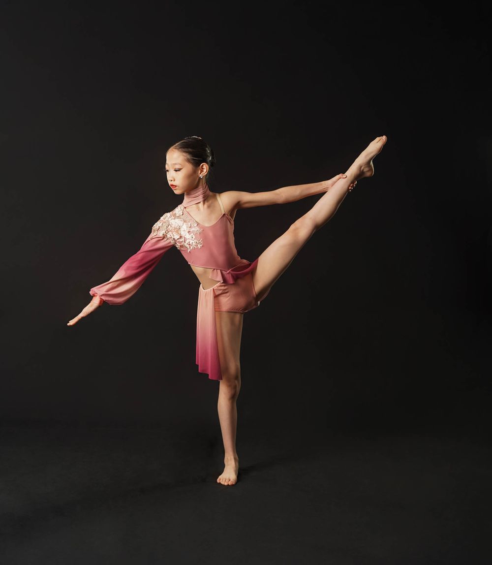 A dancer in a pink costume demonstrates perfect form in an arabesque pose.