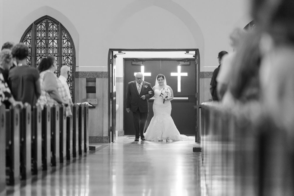 A black and white photo of a wedding ceremony inside a church with gothic architecture and illuminated crosses.