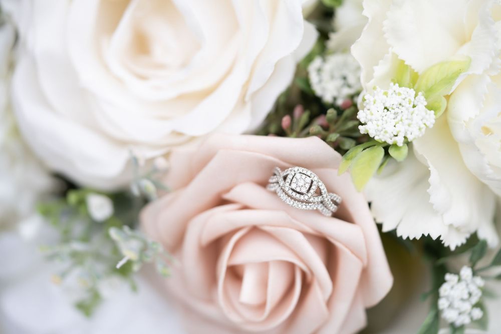 A diamond engagement ring nestled among soft pink and white roses with delicate baby's breath.