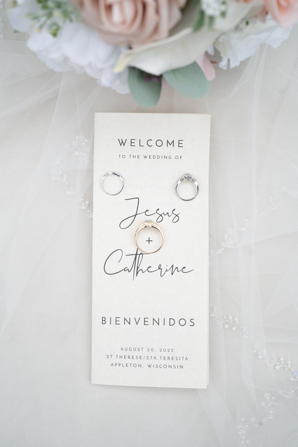 Wedding welcome sign with rings displayed on white paper surrounded by pink roses.
