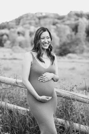 Person in fitted dress poses against mountain backdrop during maternity photoshoot.