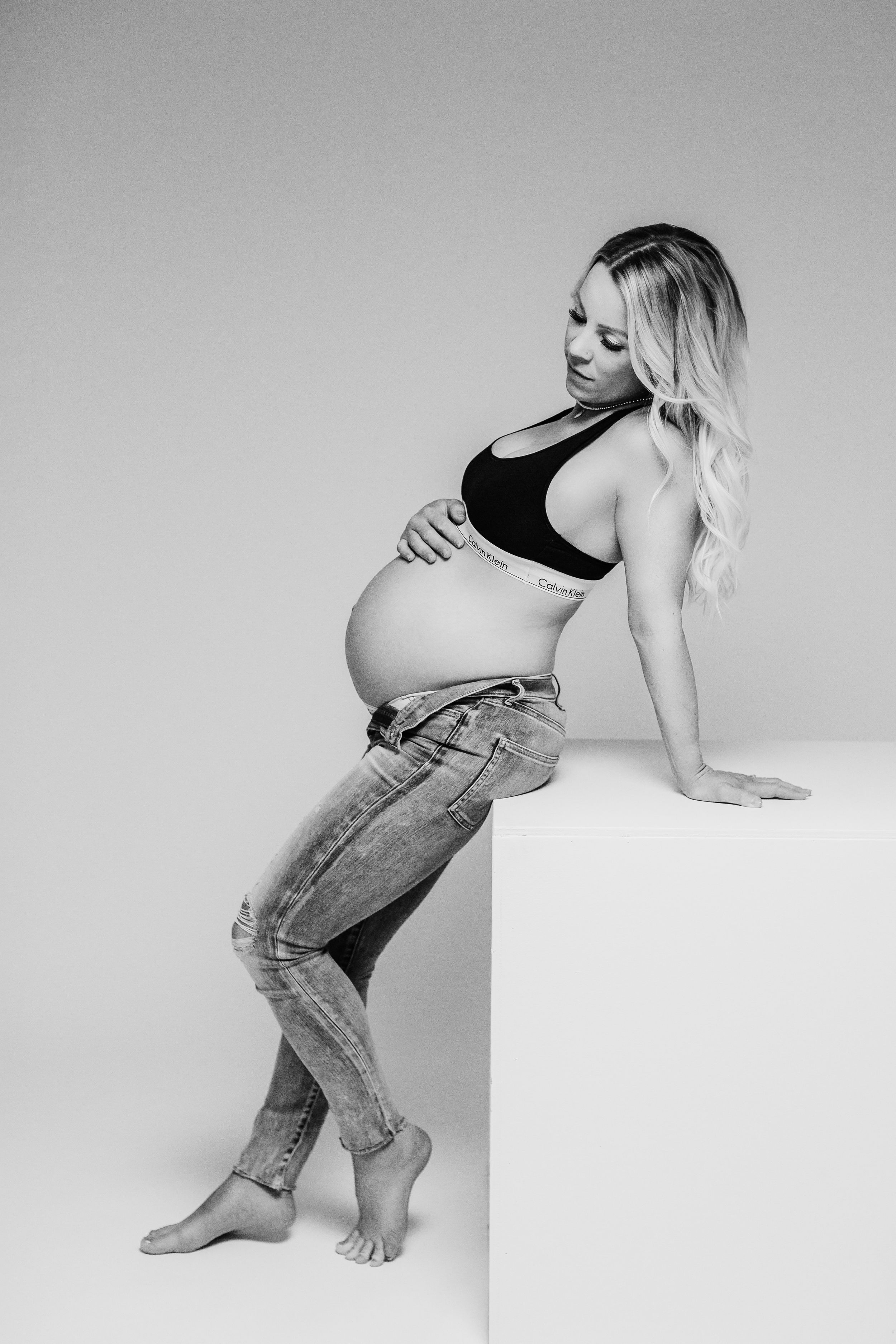 Black and white portrait of an expectant mother in casual attire posing against a light background.