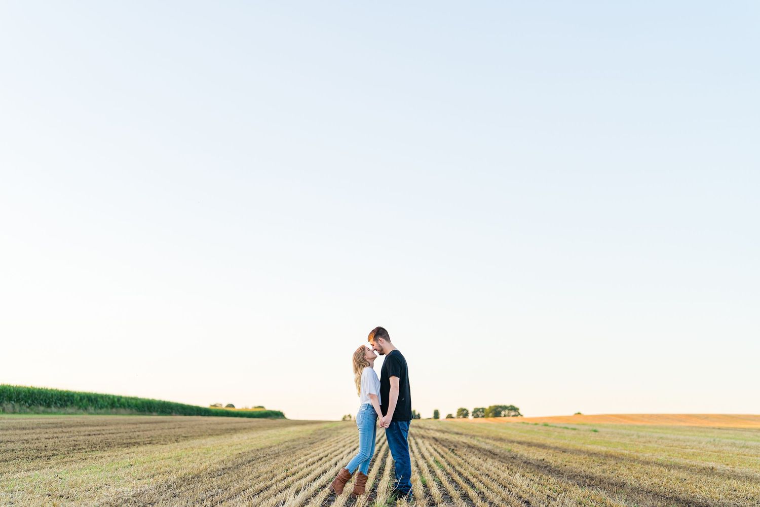A couple embraces in an open field during golden hour.