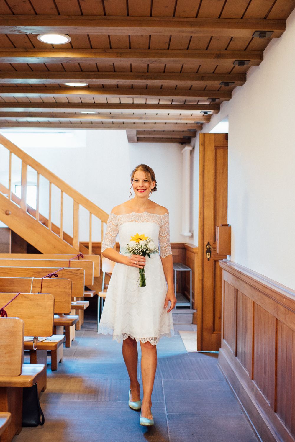 Light-filled church corridor with wooden pews and beamed ceiling.