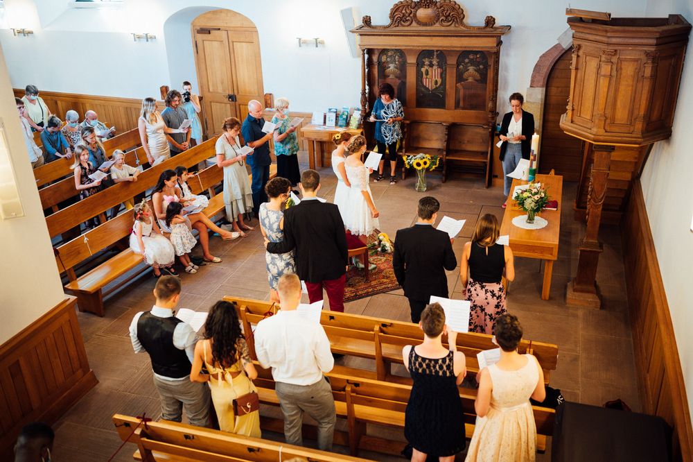 Wedding ceremony attendees seated in wooden church pews with antique wood furniture and decor.