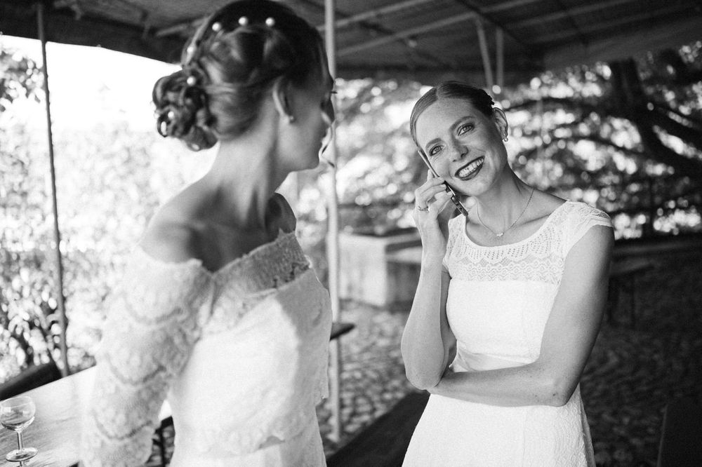 Two women in white dresses share a candid moment outdoors.