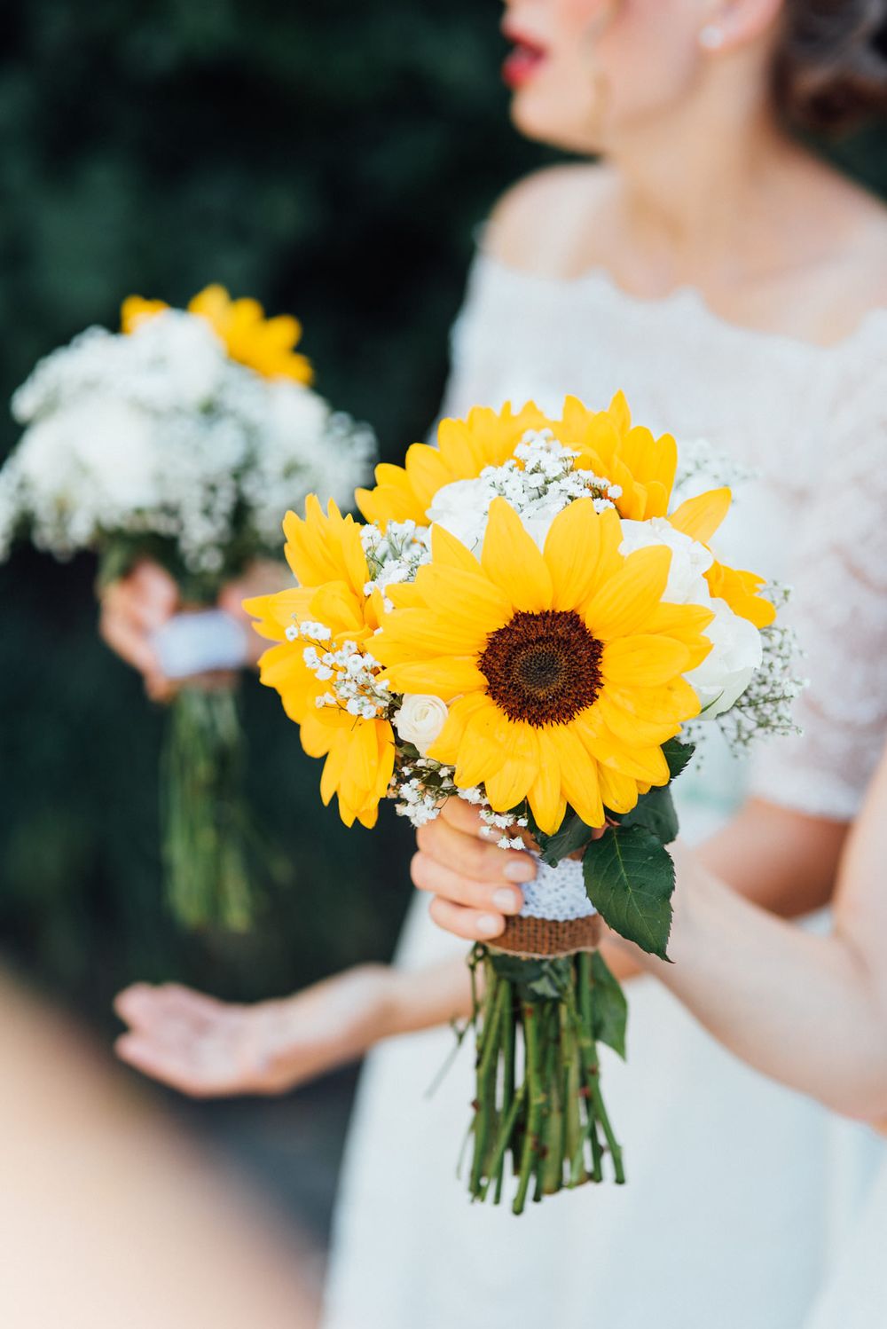 Bright yellow sunflower bouquet with baby's breath held against a white dress.