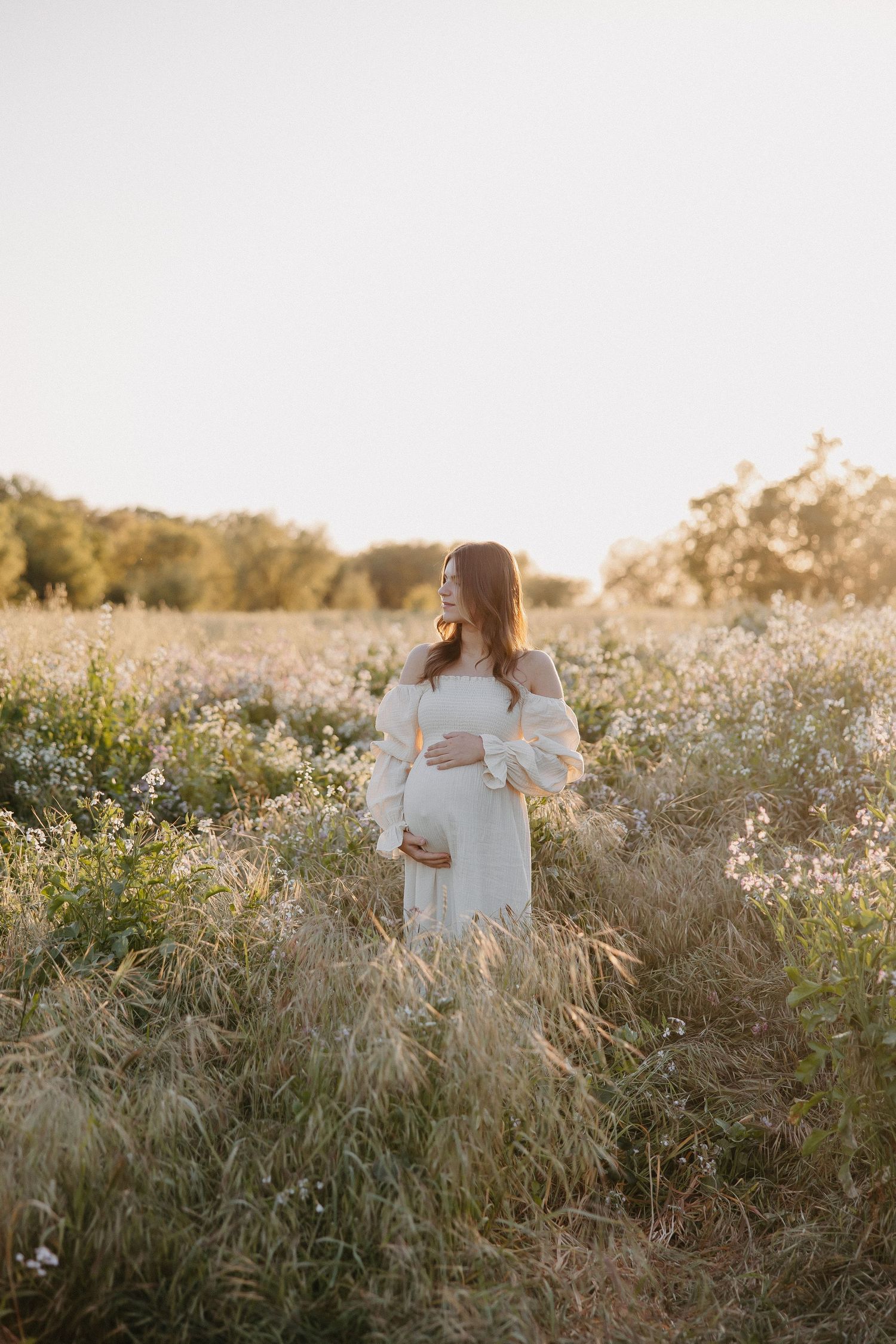 Gentle maternity moment captured in field of wildflowers during sunset.