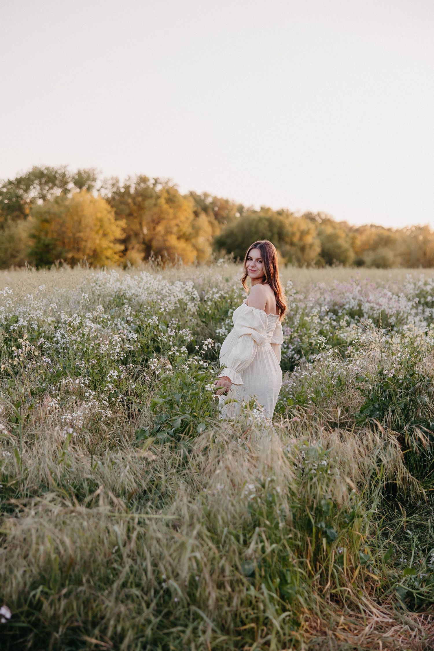 Dreamy maternity photo captures woman in off-shoulder dress among wildflowers.