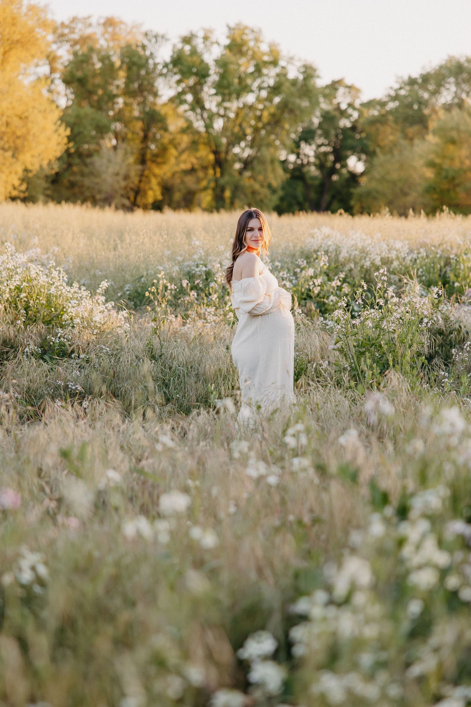 Side profile maternity shot in flowing white dress surrounded by wild daisies.