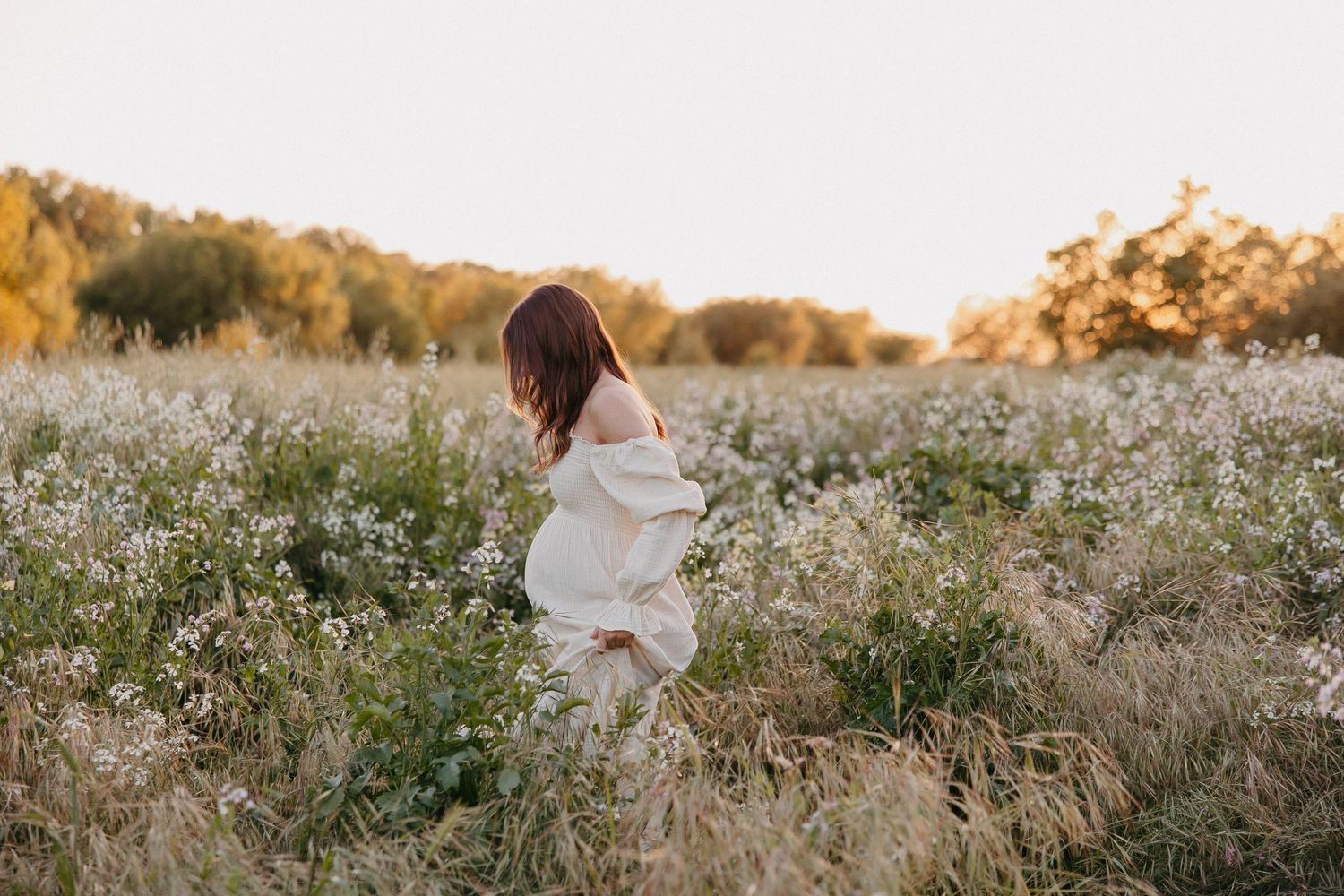 Woman in ethereal white dress twirls through field of wildflowers at golden hour.