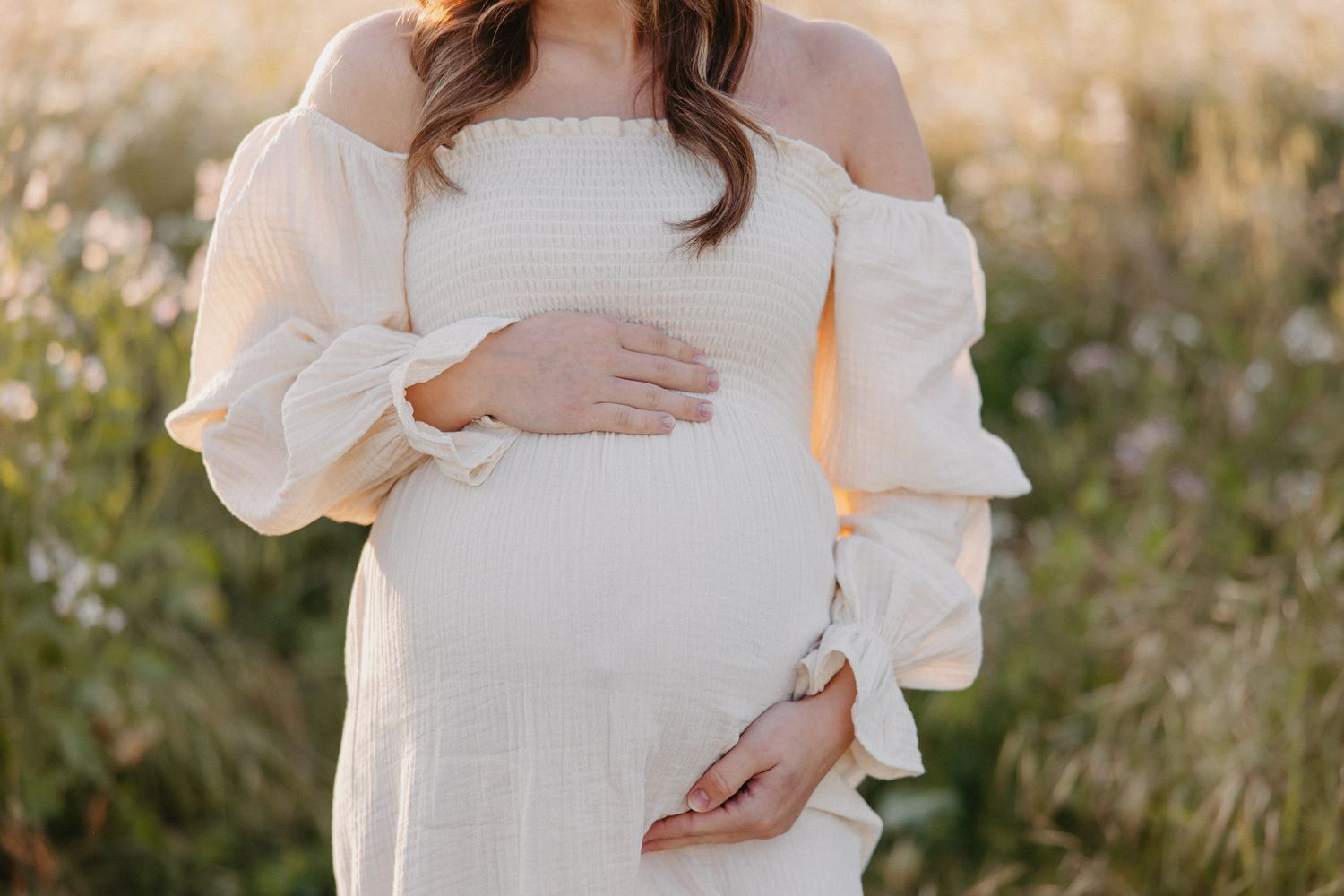 Close-up of flowing white maternity dress with billowing sleeves in natural outdoor setting.