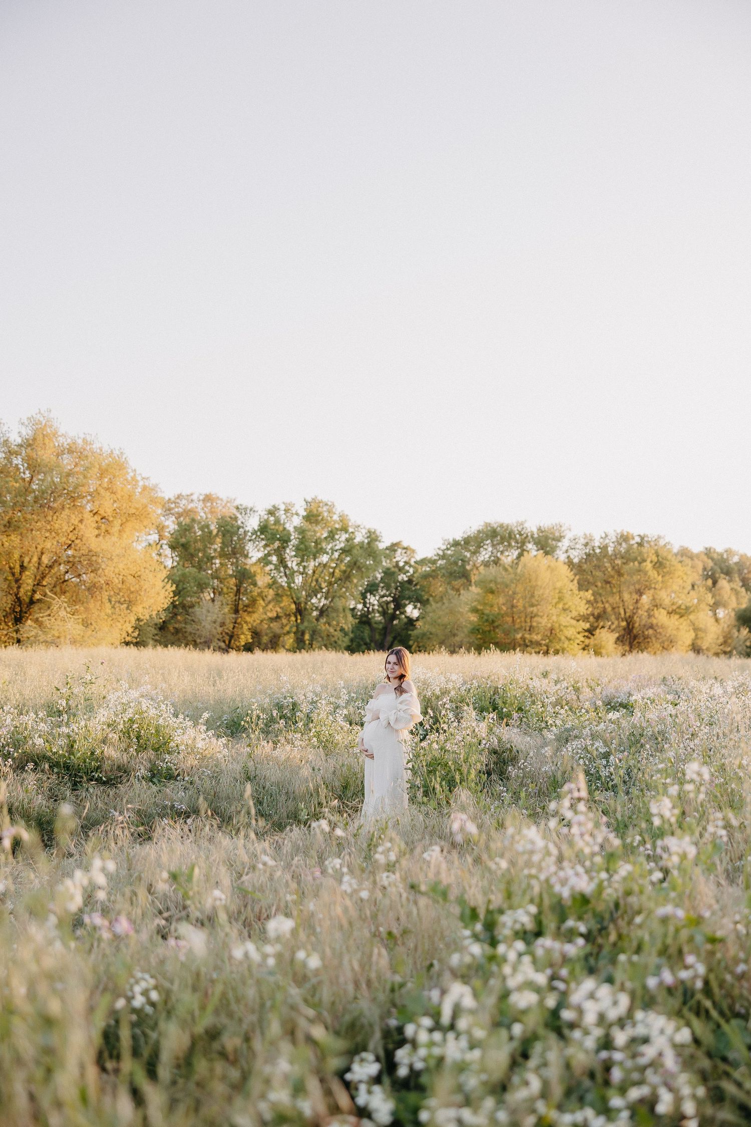 Wide landscape view of maternity photoshoot in flowering meadow with golden trees.