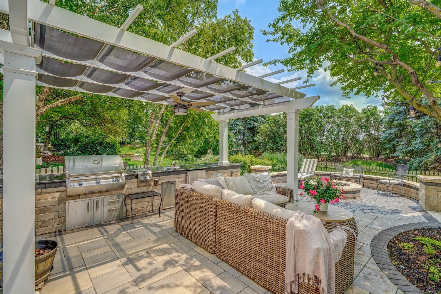 Modern outdoor kitchen and dining area with pergola cover and wicker furniture.
