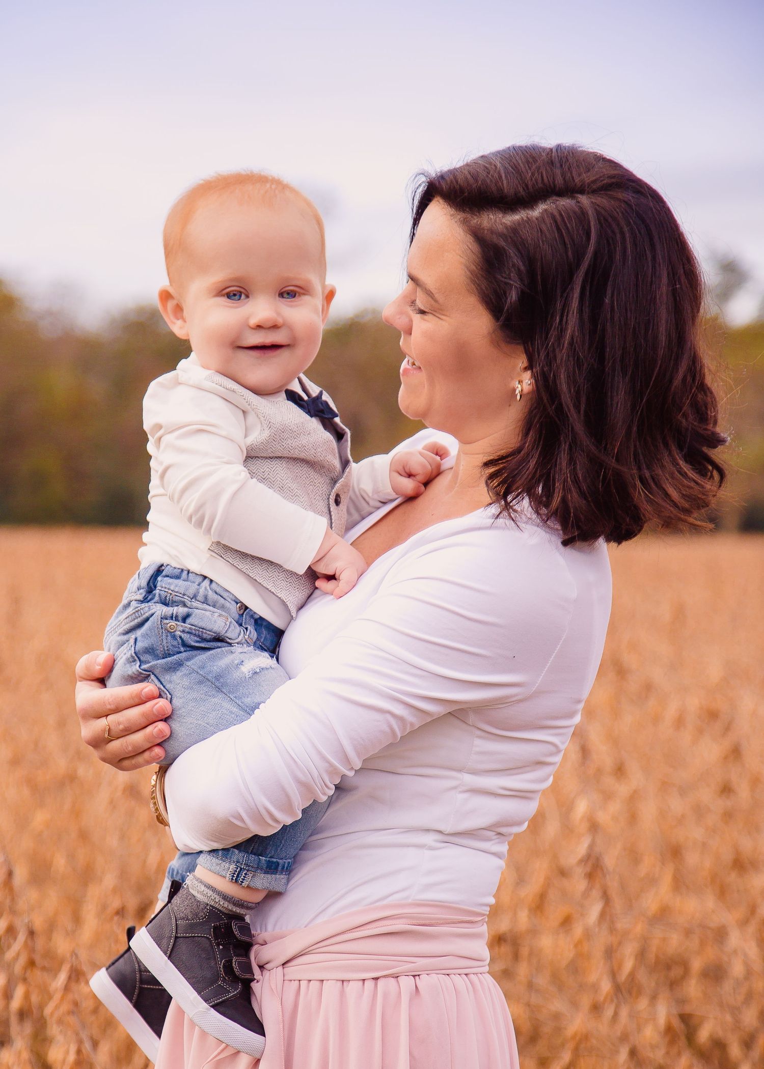 Loving mother holding smiling red-haired baby boy in golden autumn field outdoors.