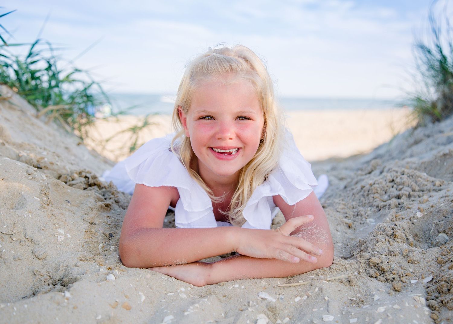 Happy blonde girl smiling while lying in sand dunes at the beach on a sunny day.