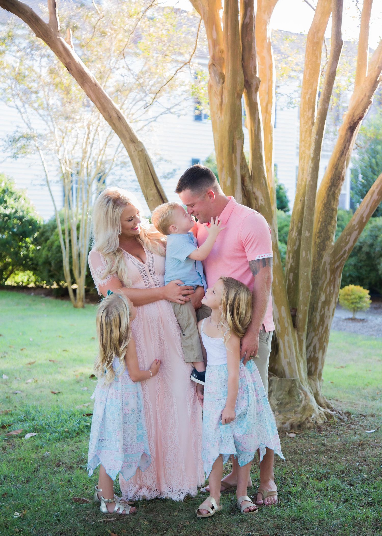 Family of five sharing a tender moment together under trees in a sunny backyard.