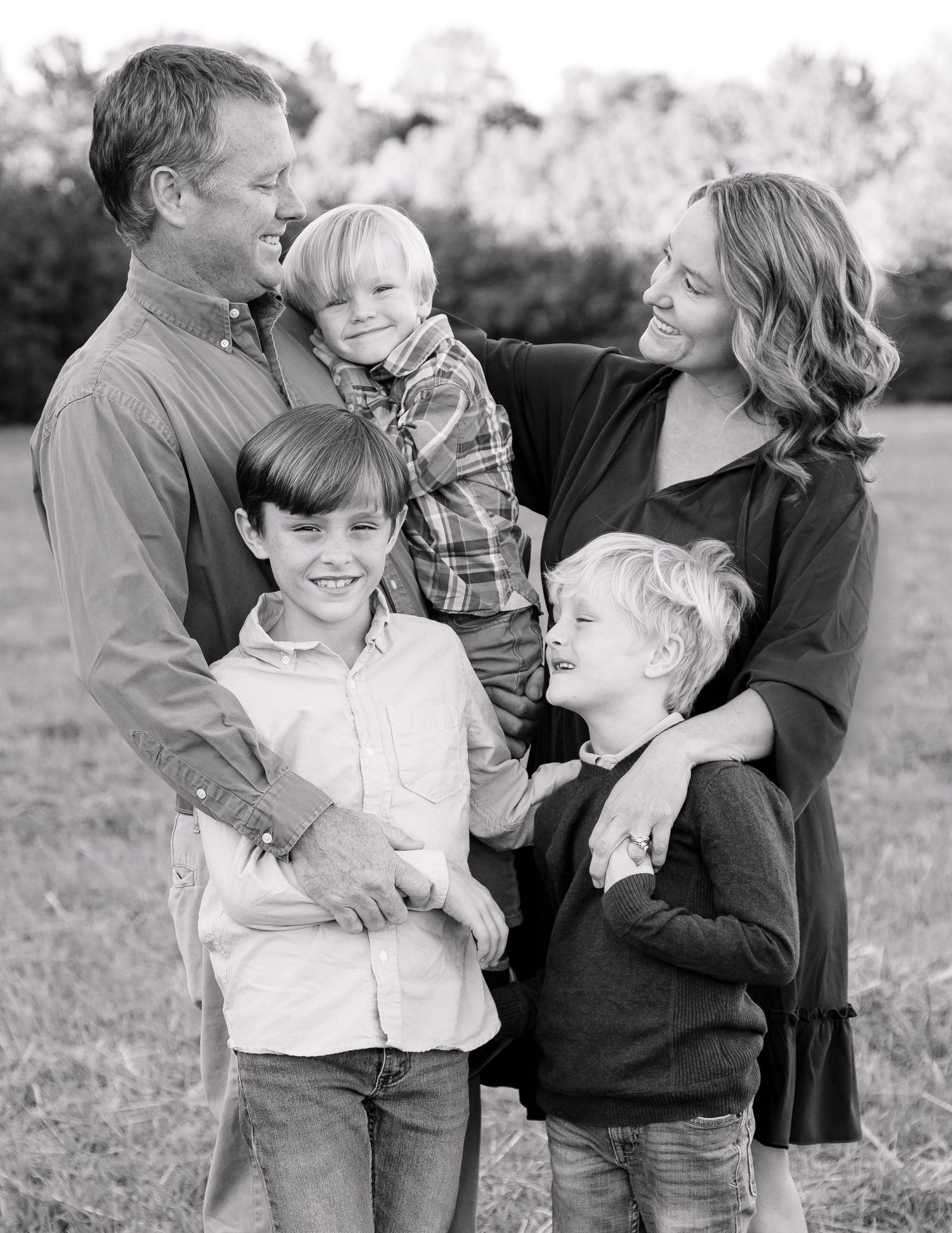 Black and white portrait of a loving family of five smiling together in an open field.