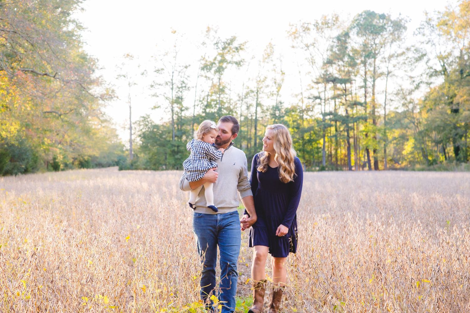 Happy young family with baby walking through a golden meadow surrounded by autumn trees.