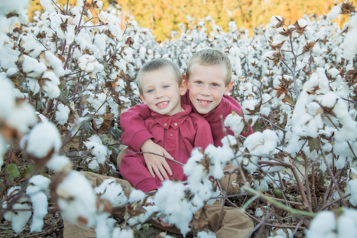 Two young siblings in red outfits smiling together in a blooming cotton field.