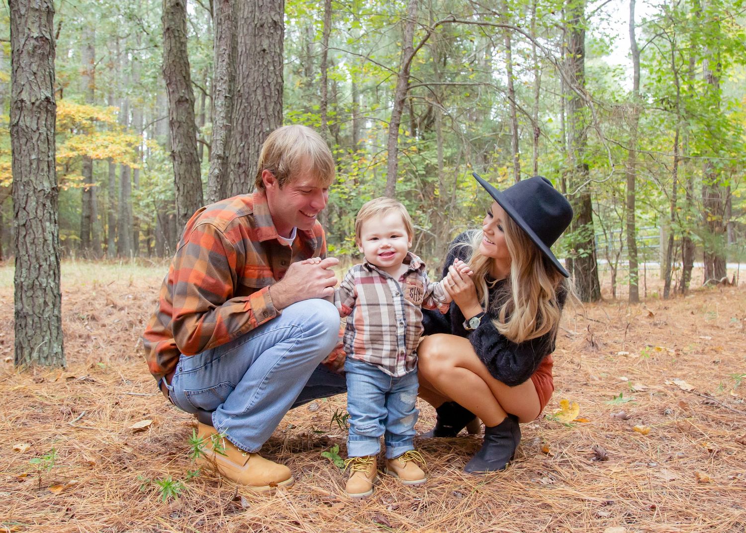 Young family of three sharing a joyful moment together in a pine forest during fall.