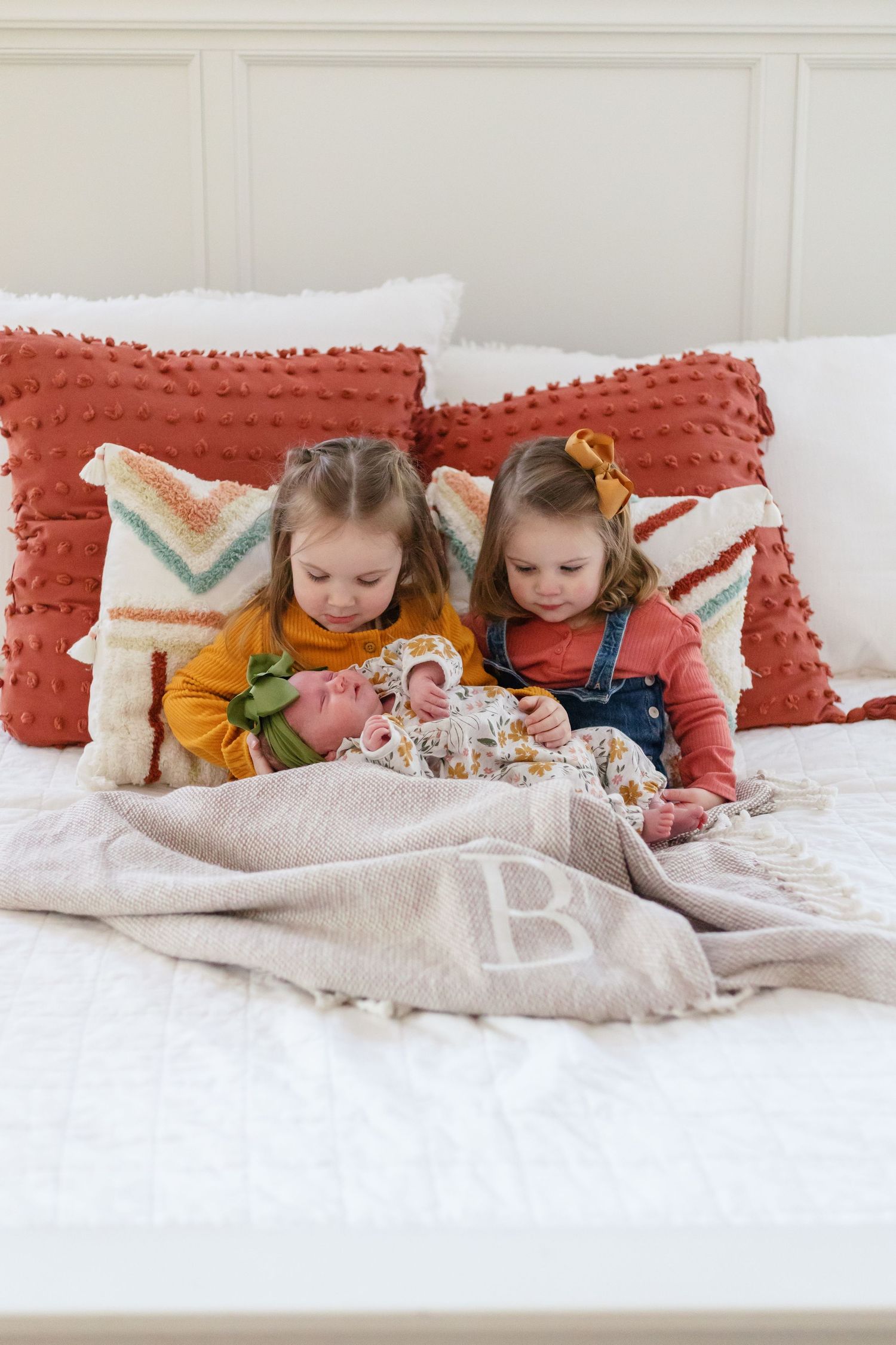 Two children read together on a bed with coral pillows and patterned blankets.