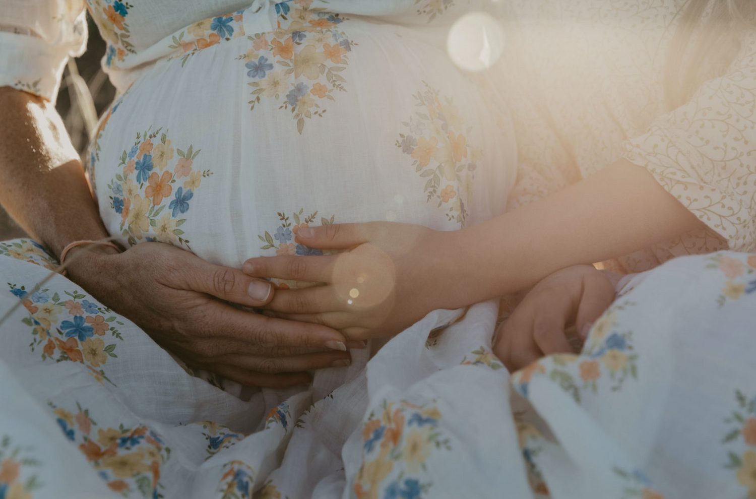 Mother and child hold pregnant belly.  On beach at sunset in Byron Bay.