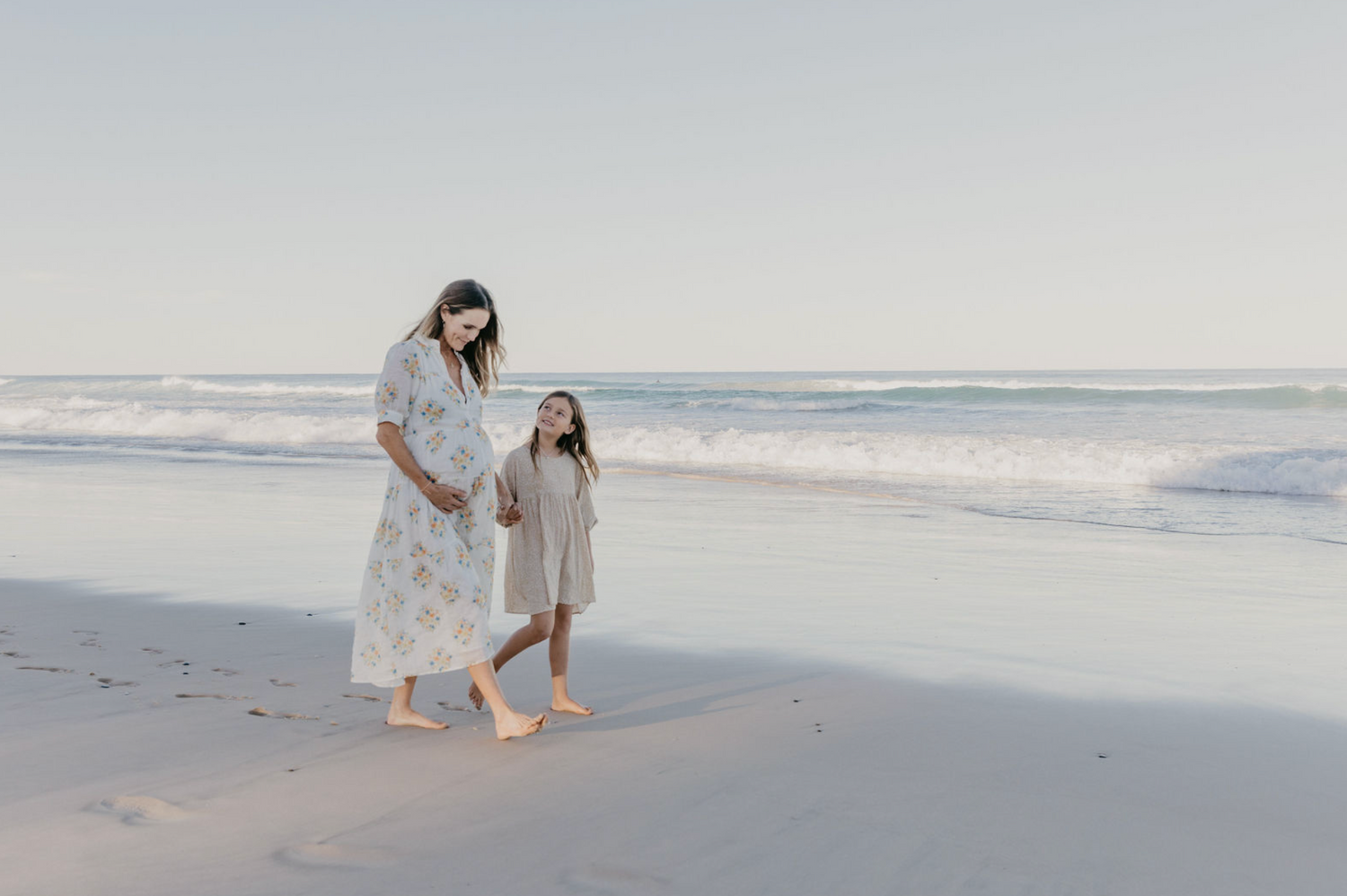 Pregnant mother and child walking down beach on sunset in Byron Bay.
